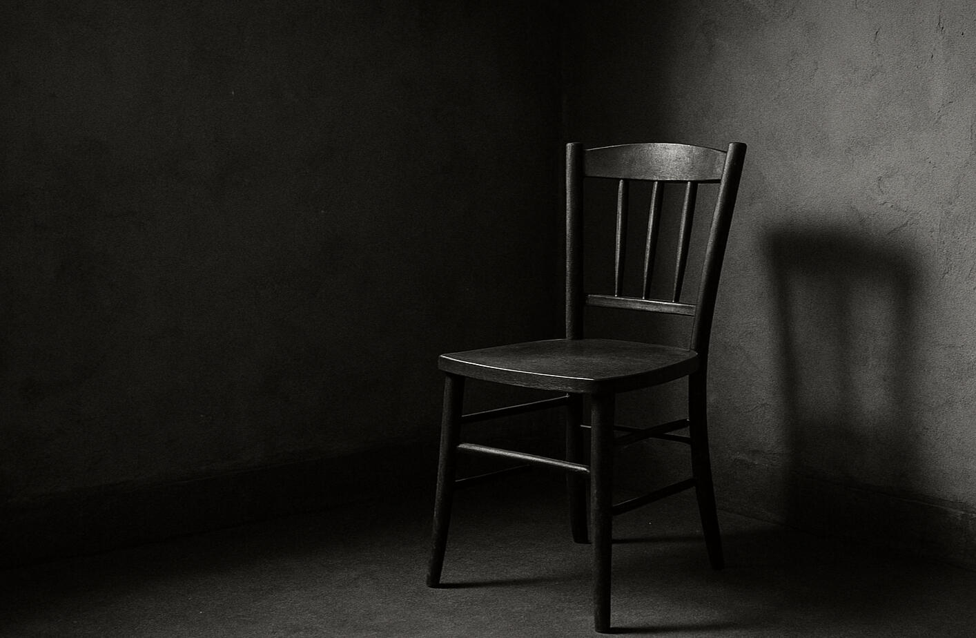 Grayscale photo of an empty wooden chair in shadow A black and white image of a solitary chair casting a long shadow against a textured wall.